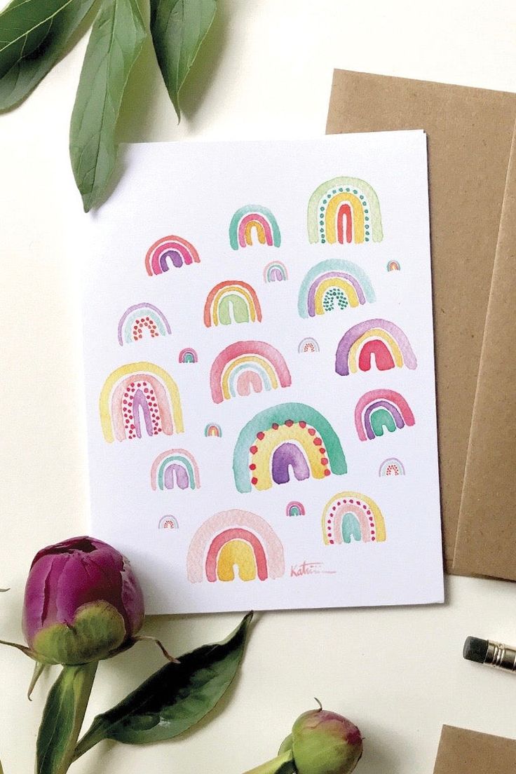 a card with rainbows on it next to some flowers and two envelopes that say happy birthday