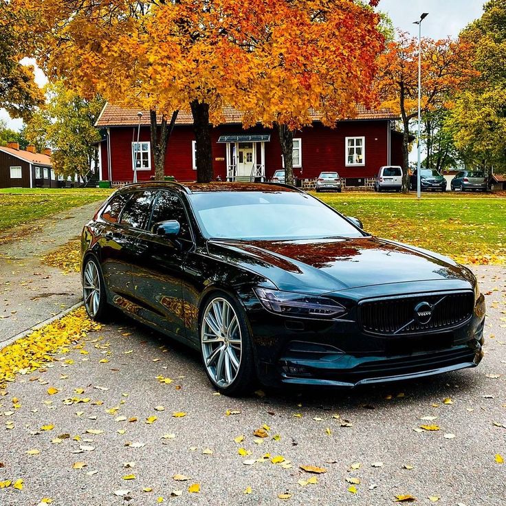 a black car parked in front of a red house with autumn leaves on the ground