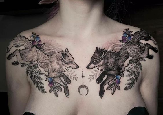 a woman with tattoos on her chest has two wolfs in the middle of it