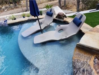 an outdoor swimming pool with lounge chairs, umbrellas and artificial grass in the background