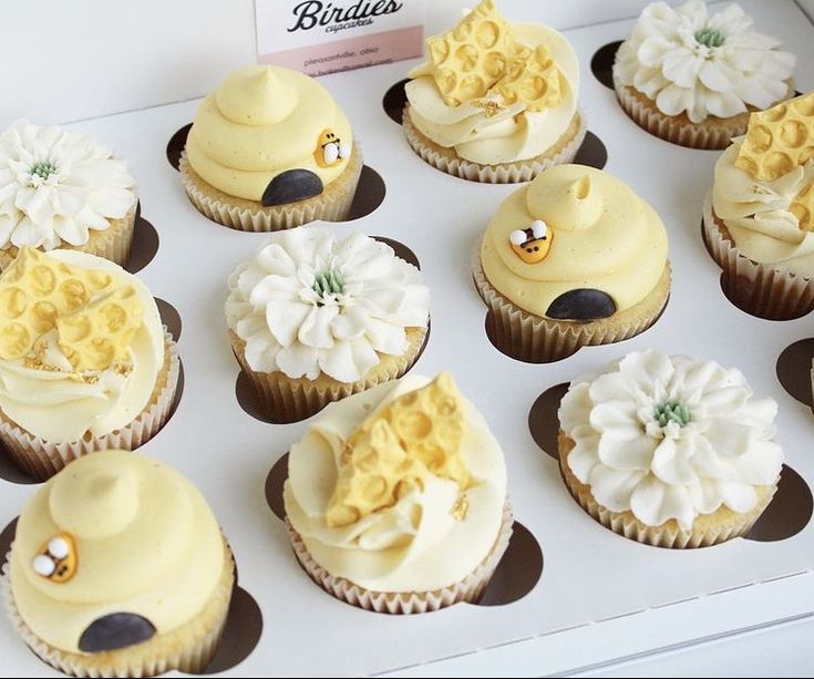 twelve cupcakes with yellow frosting and white flowers on them are in a box