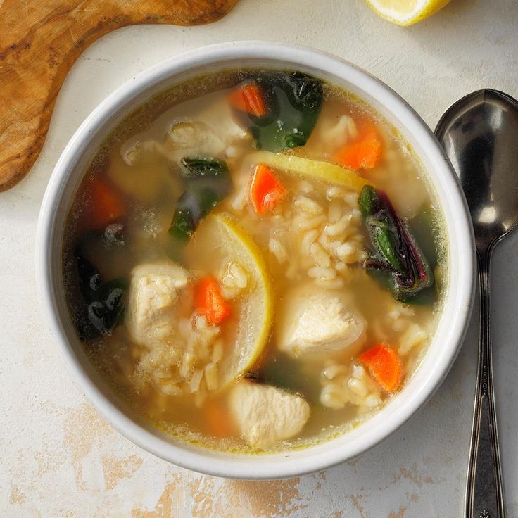 a white bowl filled with chicken, rice and carrots next to a slice of lemon