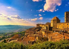 an old village is surrounded by hills and trees on a sunny day with clouds in the sky