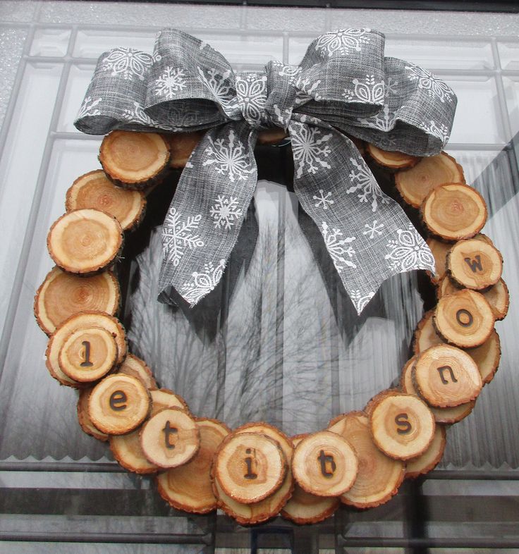 a wreath made out of logs with the word joy on it and a bow hanging from the front door