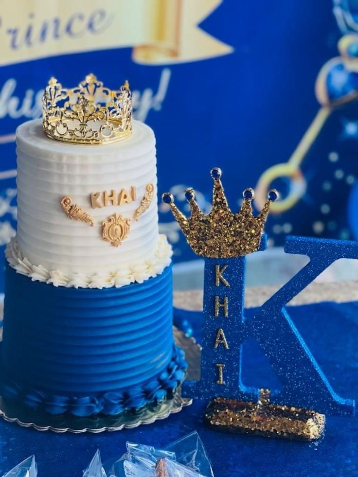 a blue and white cake with a crown on top next to a small letter k