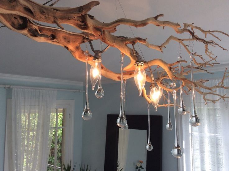 a chandelier made out of branches and hanging lights in a room with windows