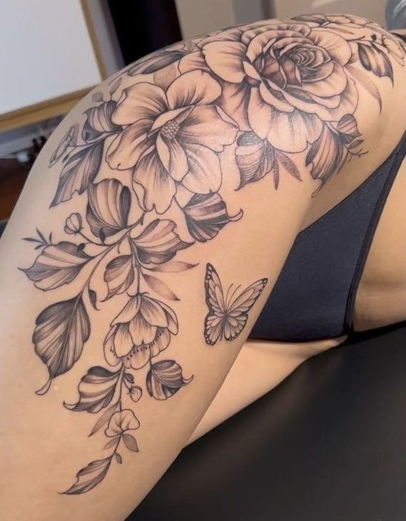 a woman's back with flowers and butterflies on her thigh, as well as an arm tattoo