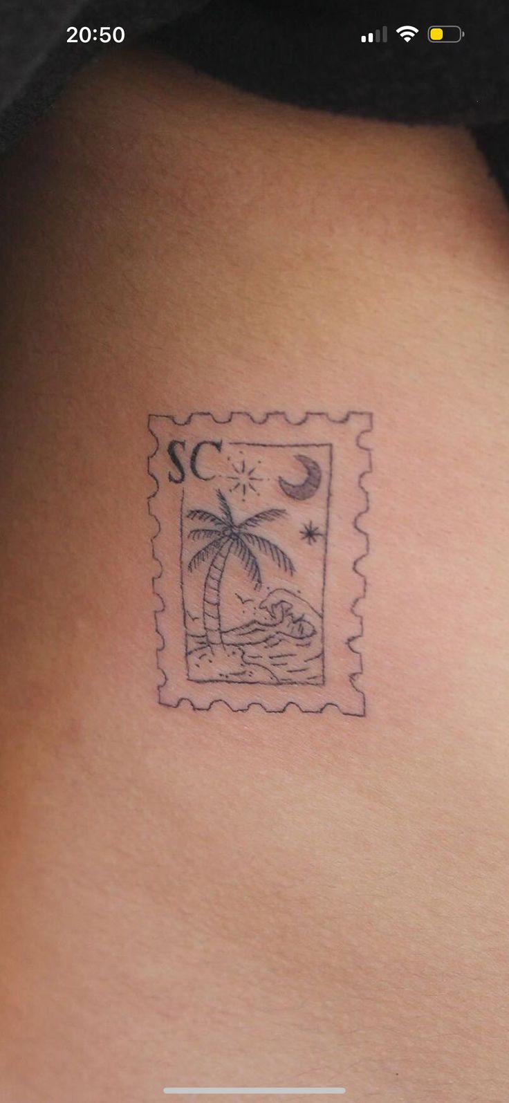 a small tattoo on the back of a woman's upper arm, depicting a stamp with a palm tree and moon