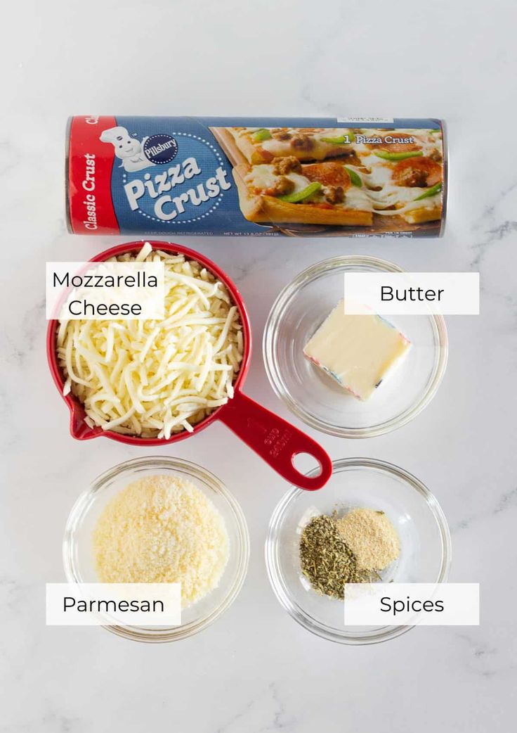 ingredients to make pizza crust laid out on a white marble counter top, including cheese, parmesan and seasoning