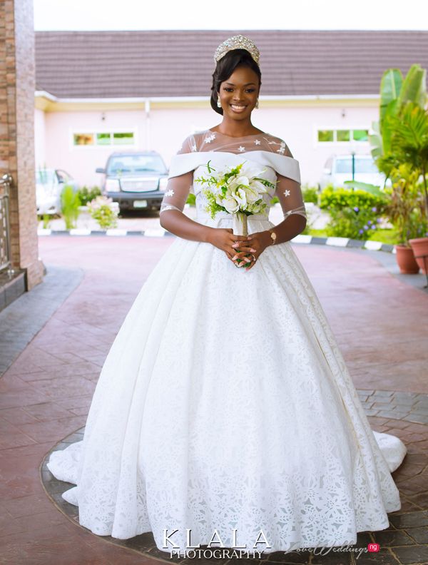 a woman in a white wedding dress standing on a brick walkway wearing a tiara and holding a bouquet