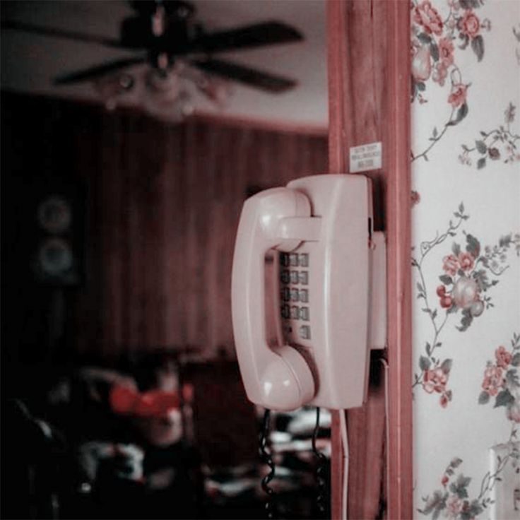 an old style phone is hanging on the wall next to a flowered wallpaper