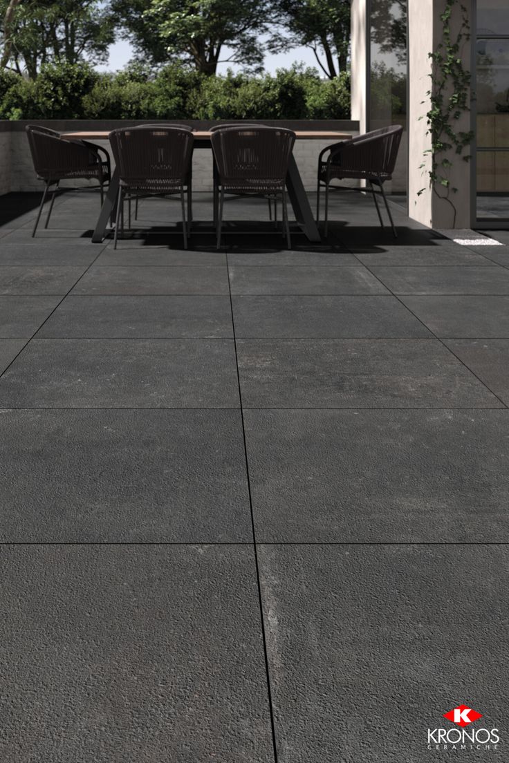 a table and chairs sitting on top of a cement floor next to a building with trees in the background