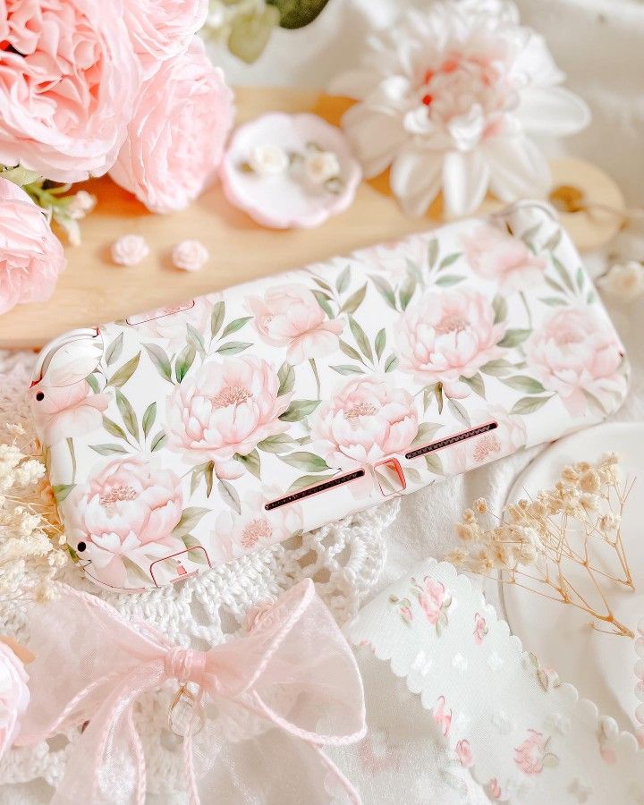 a pink flowered purse sitting on top of a white bed next to some flowers