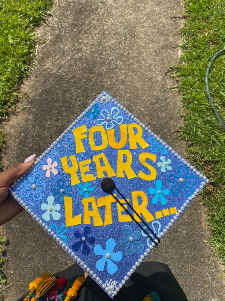 a blue graduation cap with four years later written on it and flowers in the center