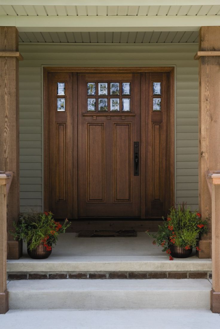 a wooden door with two planters on the front steps and sidelights above it