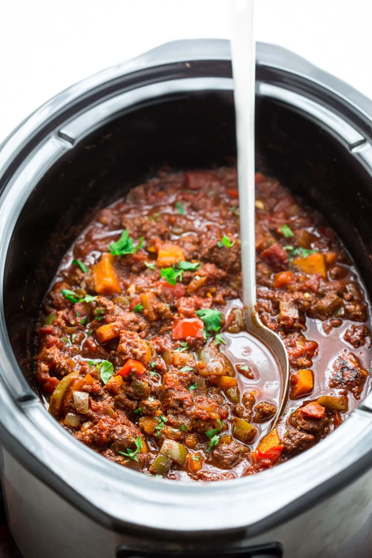 a slow cooker filled with meat and vegetables being spooned into it by a ladle