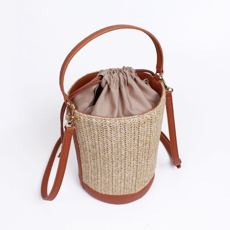 Made from high quality Raffia. Vegan leather trim. Polyester lining. Our raffia line are all made with an interior liner to keep your items safe and enclosed from beach sand or any harsh environment. Great size for traveling and for the summer heat.  Detachable shoulder strap included. Dimensions: 150x215X150mm Weight:  286g (bag) SHIPPING:  Free shipping from South Korea, estimated 7-14 days to get to you from purchase date.  RETURNS:  Return address is in USA so that returns can be made and given fast.  Returns up to 2 weeks starting when the shipping is completed.  Returns must be with tags.  Buyer must pay for return shipping unless item was damaged or incorrect.  Money will be refunded after we receive and inspect the item. Orders over $250 will have to pay 20% restocking fee. Eco-friendly Woven Leather Crochet Bucket Bag, Natural Jute Bucket Bag With Braided Handles, Eco-friendly Woven Leather Bucket Bag, Brown Bamboo Handle Bucket Shoulder Bag, Chic Beige Woven Leather Bucket Bag, Brown Straw Bag With Bamboo Handle In Bucket Shape, Brown Woven Rattan Bucket Bag, Chic Brown Jute Bucket Bag, Casual Woven Jute Bucket Bag