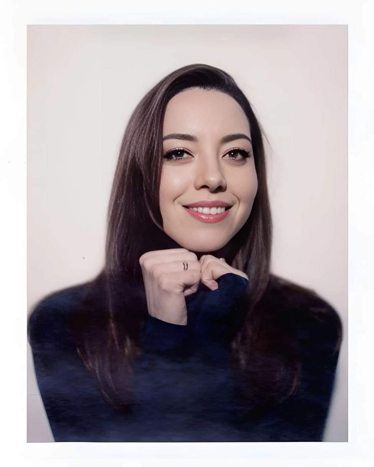 a woman with long dark hair smiling and posing for a photo in front of a white wall