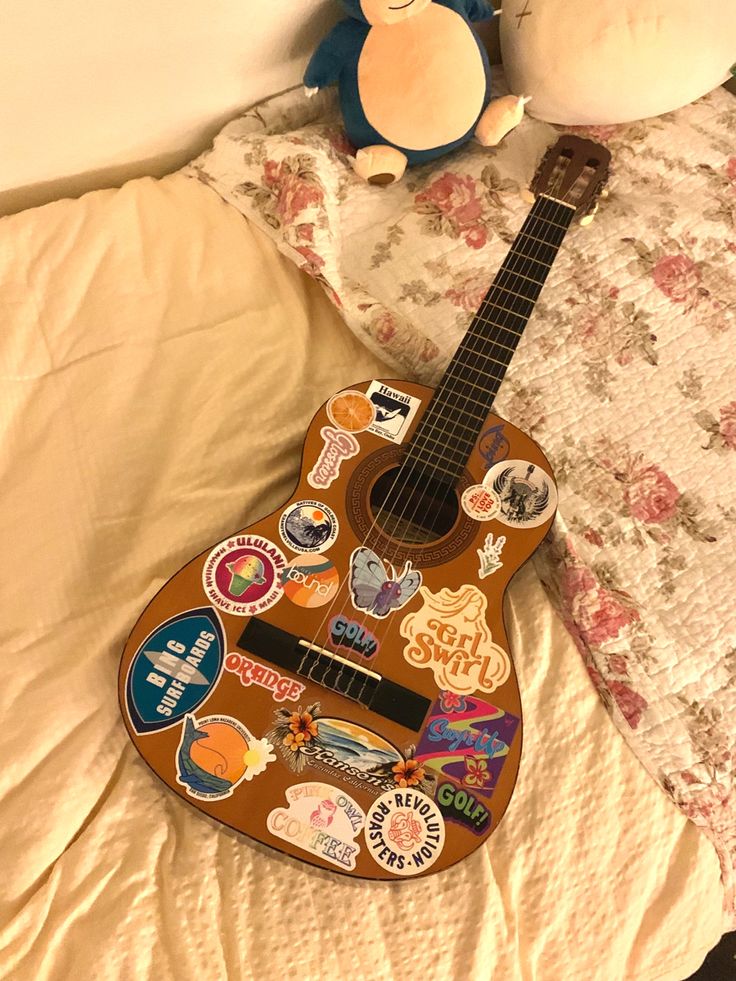 a guitar sitting on top of a bed next to a stuffed animal and pillow with stickers all over it