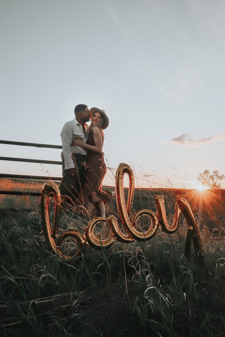 a man and woman standing next to each other in front of a wooden fence with the word love spelled out