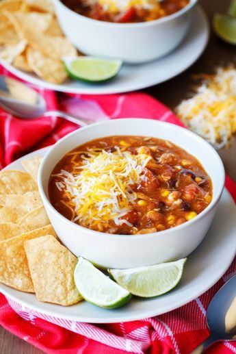 two bowls of chili with tortilla chips and limes on the side,