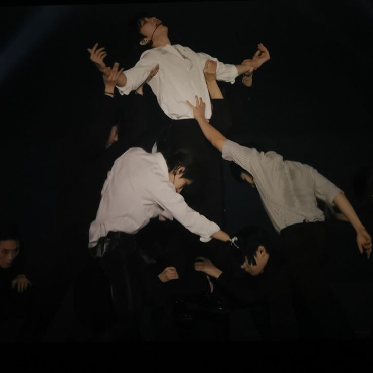 four men in white shirts and black pants are performing on stage with their hands up