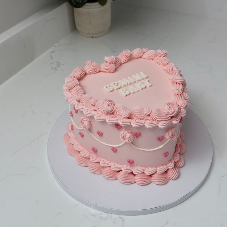 a pink heart shaped cake sitting on top of a white table next to a potted plant