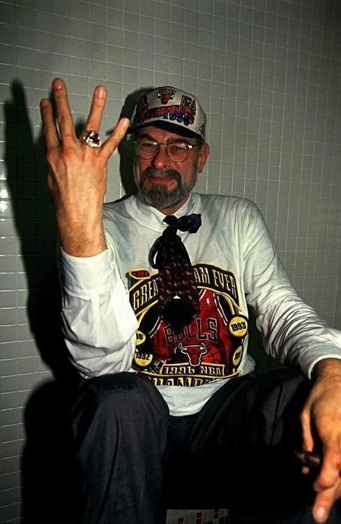 a man sitting in a chair making the peace sign with his hand and wearing a hat