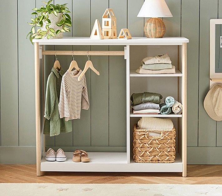 a white shelf filled with clothes next to a lamp and potted plant on top of a hard wood floor