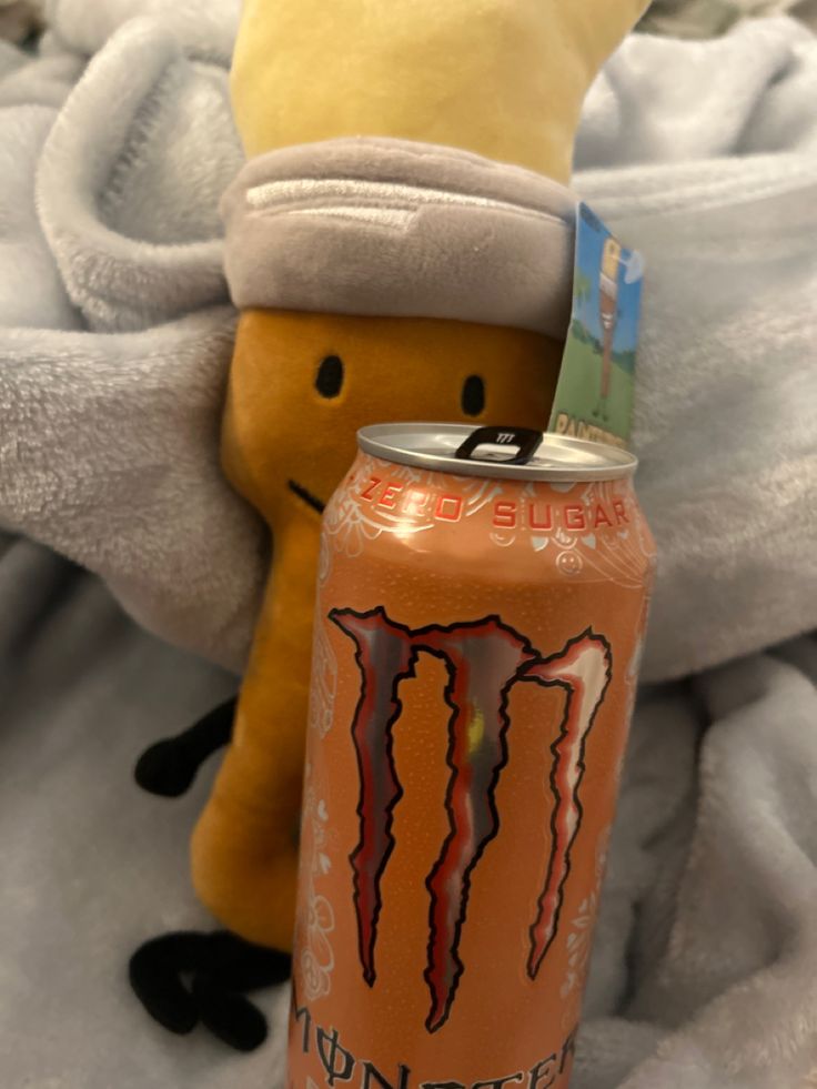 a can of monster energy drink next to a stuffed animal on top of a blanket