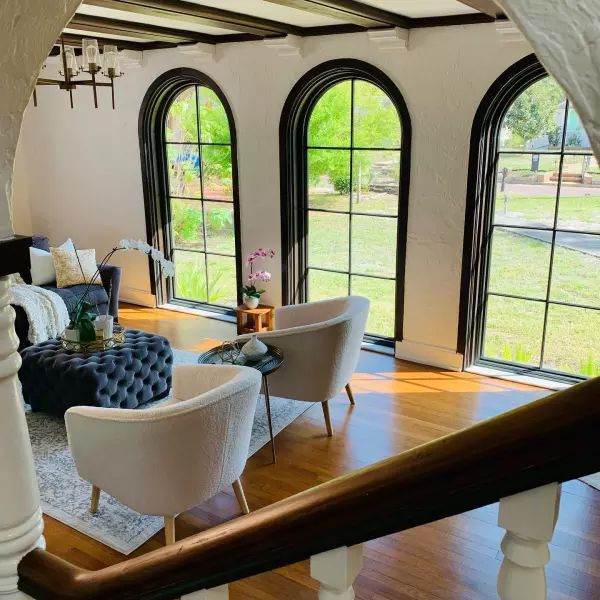 a living room filled with furniture next to two large arched windows on top of a wooden floor