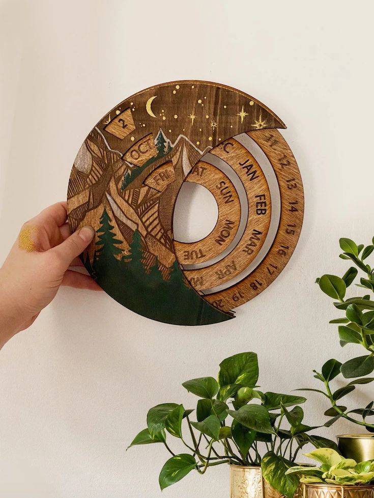 a hand holding a wooden clock on the wall next to a plant and potted plant