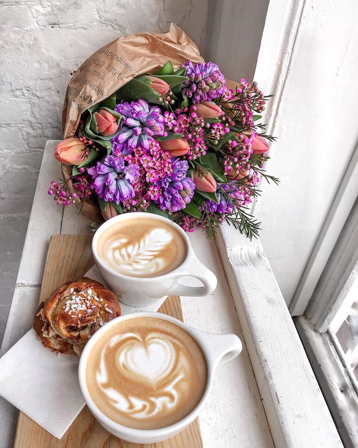 two cups of cappuccino on a table with flowers