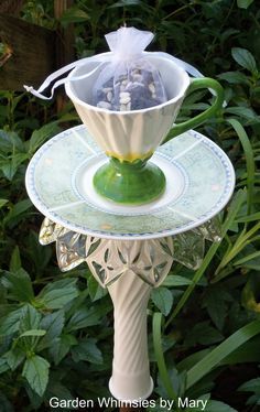 a green and white vase sitting on top of a stand in front of some plants