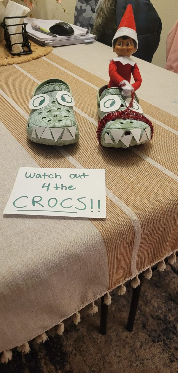 an elf sitting on top of a table next to two stuffed alligators and a sign that says watch out for the croci