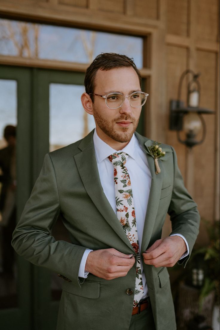 a man in a green suit and floral tie is posing for the camera with his hands on his hips