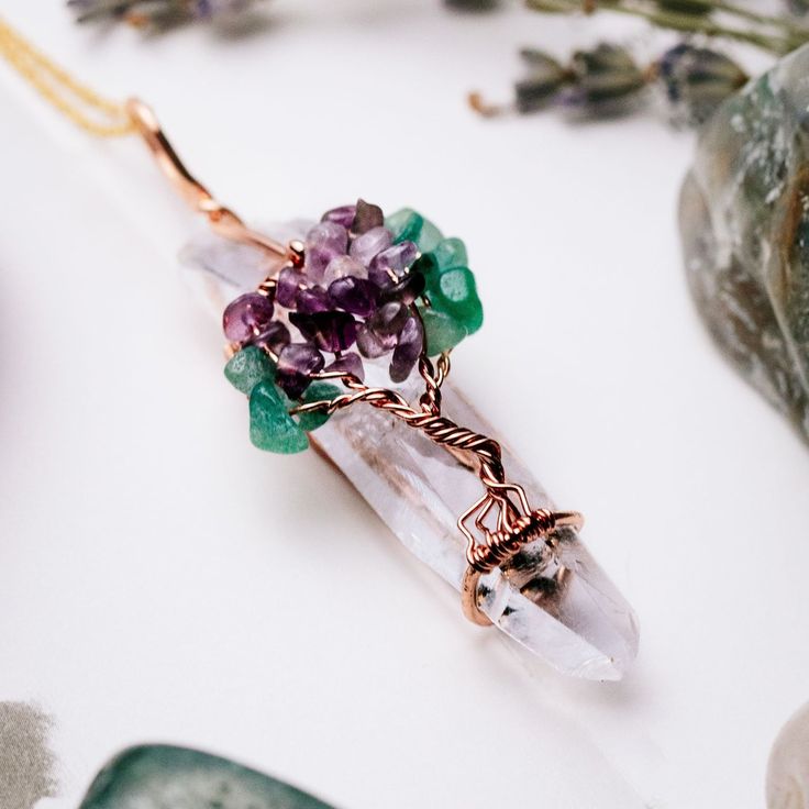 a piece of jewelry sitting on top of a table next to some rocks and flowers