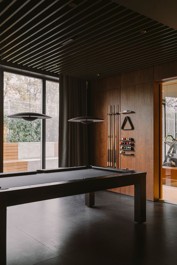 a pool table in the middle of a room with large windows and wood paneling