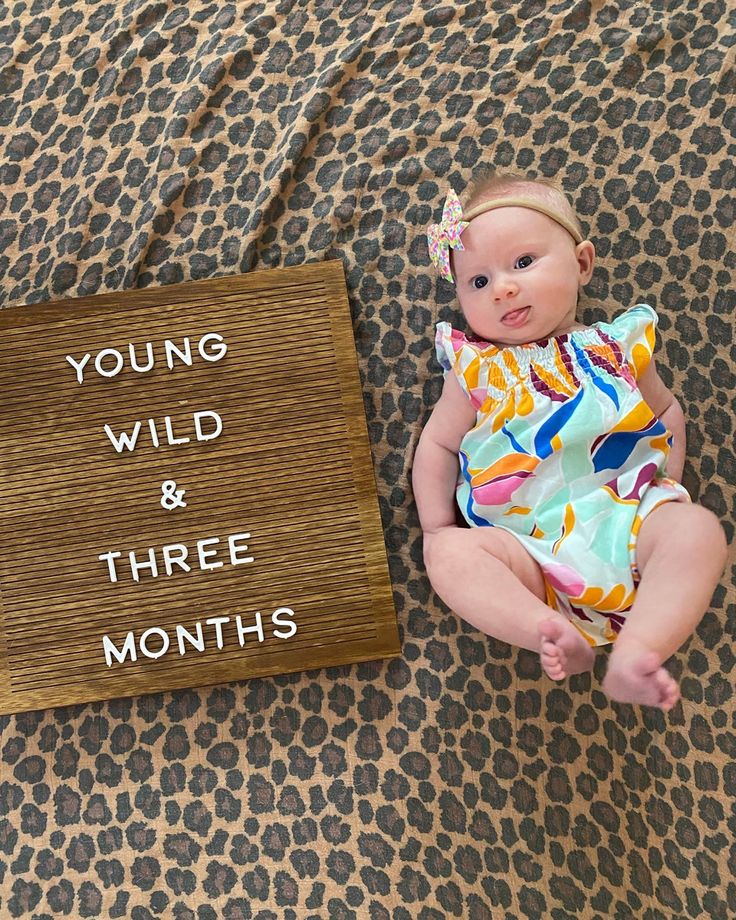 a baby is sitting next to a sign that says young wild and three months old