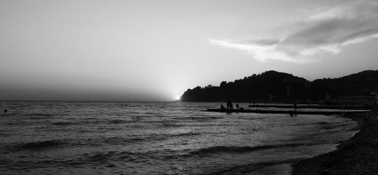 black and white photo of people on the beach at sunset with mountains in the background