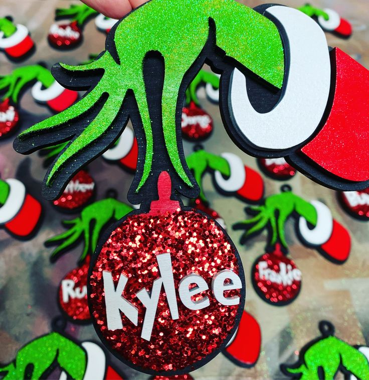 someone holding up some christmas ornaments with the word kleene on them in red, green and white glitter