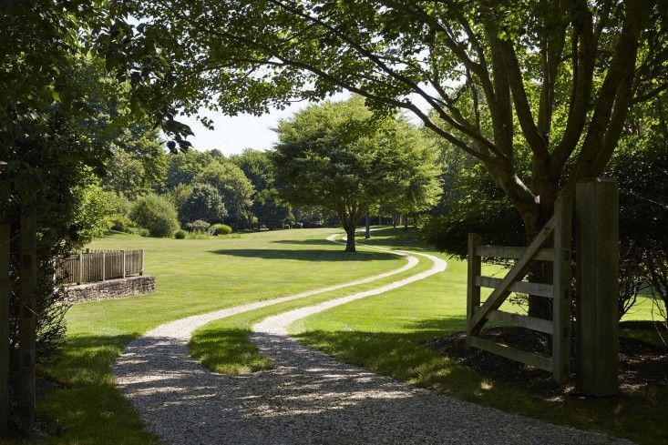 a path leading to a grassy field with trees on both sides and a wooden gate at the end