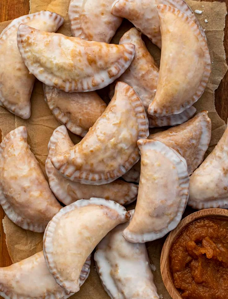 several pastries on a piece of paper next to a small bowl of dipping sauce