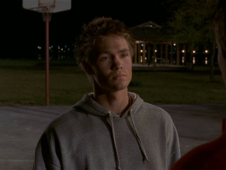 a young man standing in front of a basketball hoop at night with his eyes closed