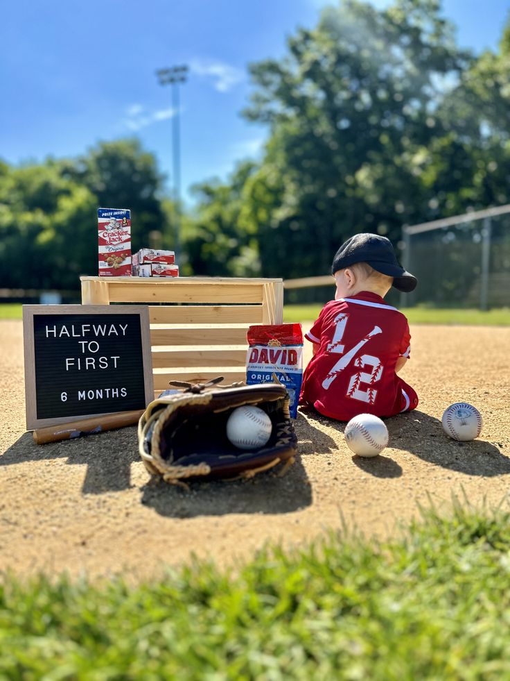 a little boy that is sitting on the ground with a baseball glove and ball in it