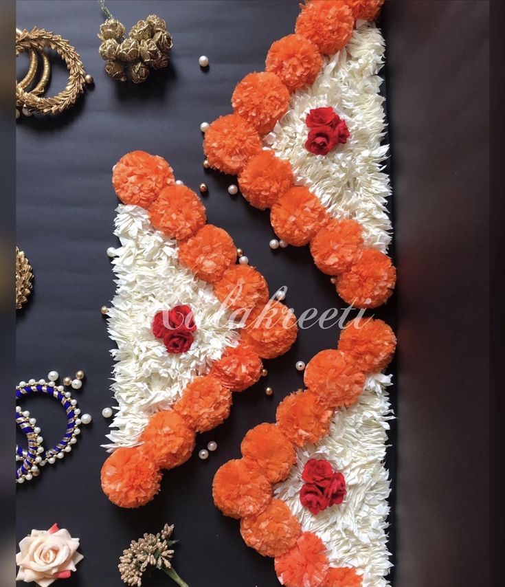 an arrangement of orange and white flowers on a black surface with pearls, necklaces and rings