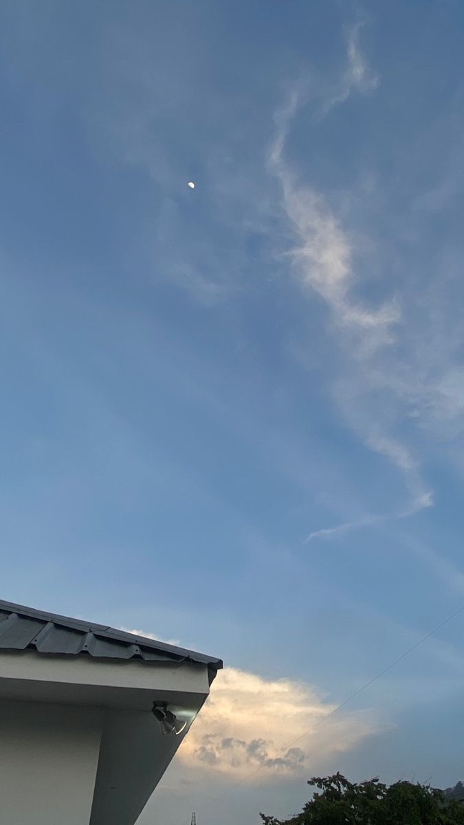 an airplane is flying high in the sky above some buildings and trees on a sunny day