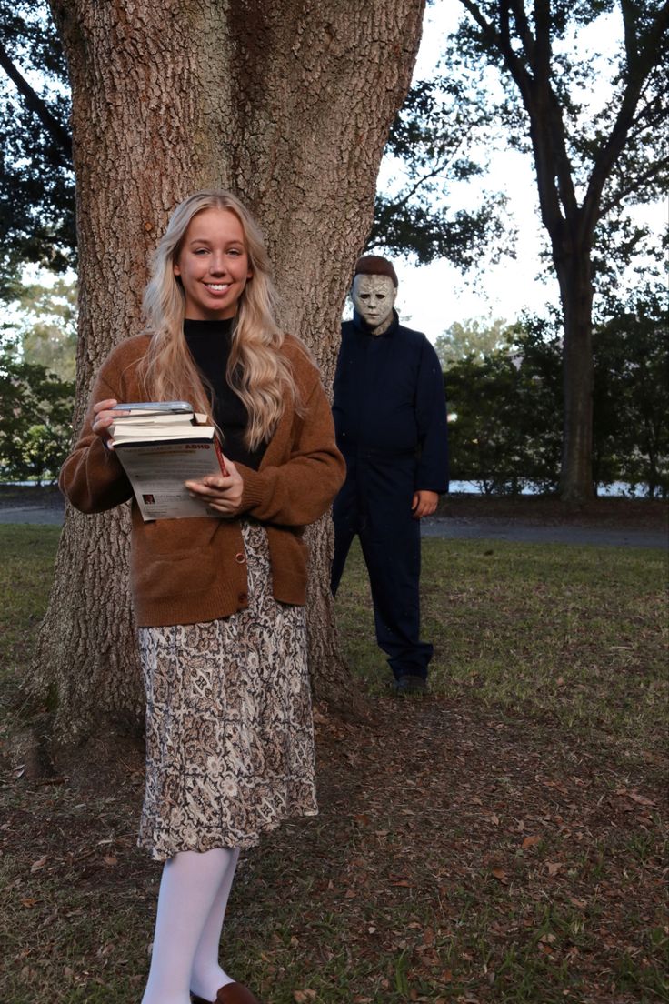 a woman standing in front of a tree with a mask on her face and holding a book