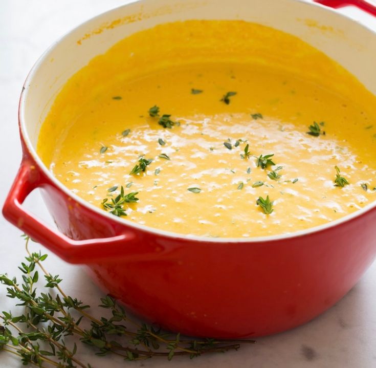 a red pot filled with soup sitting on top of a white counter next to a sprig of parsley