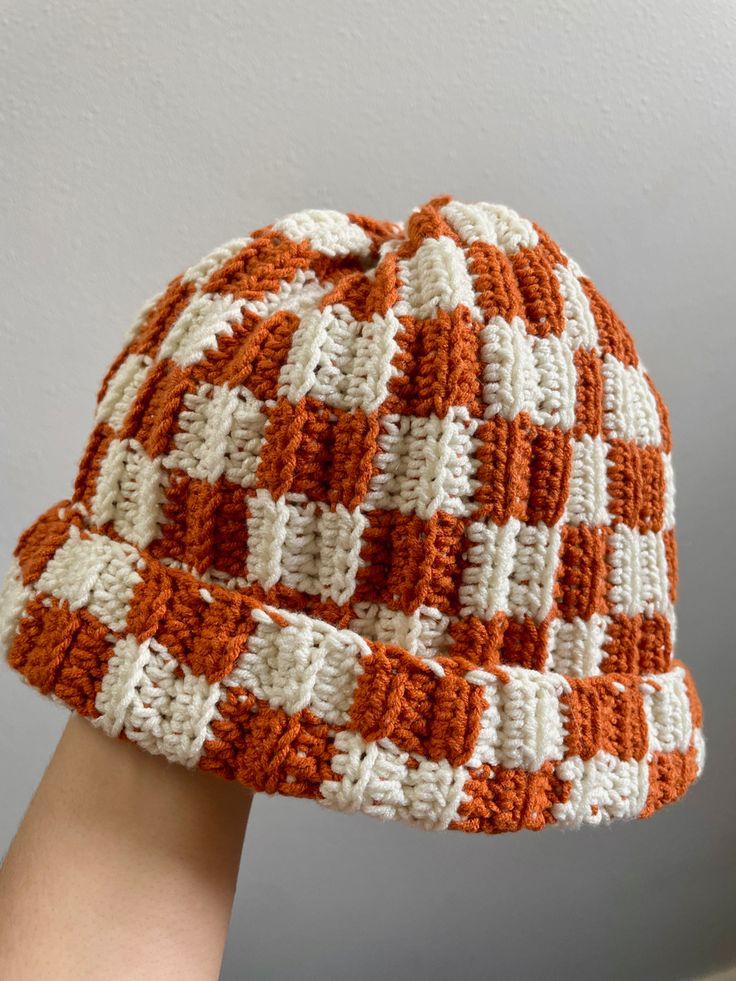 someone is wearing a crocheted hat with orange and white squares on the side